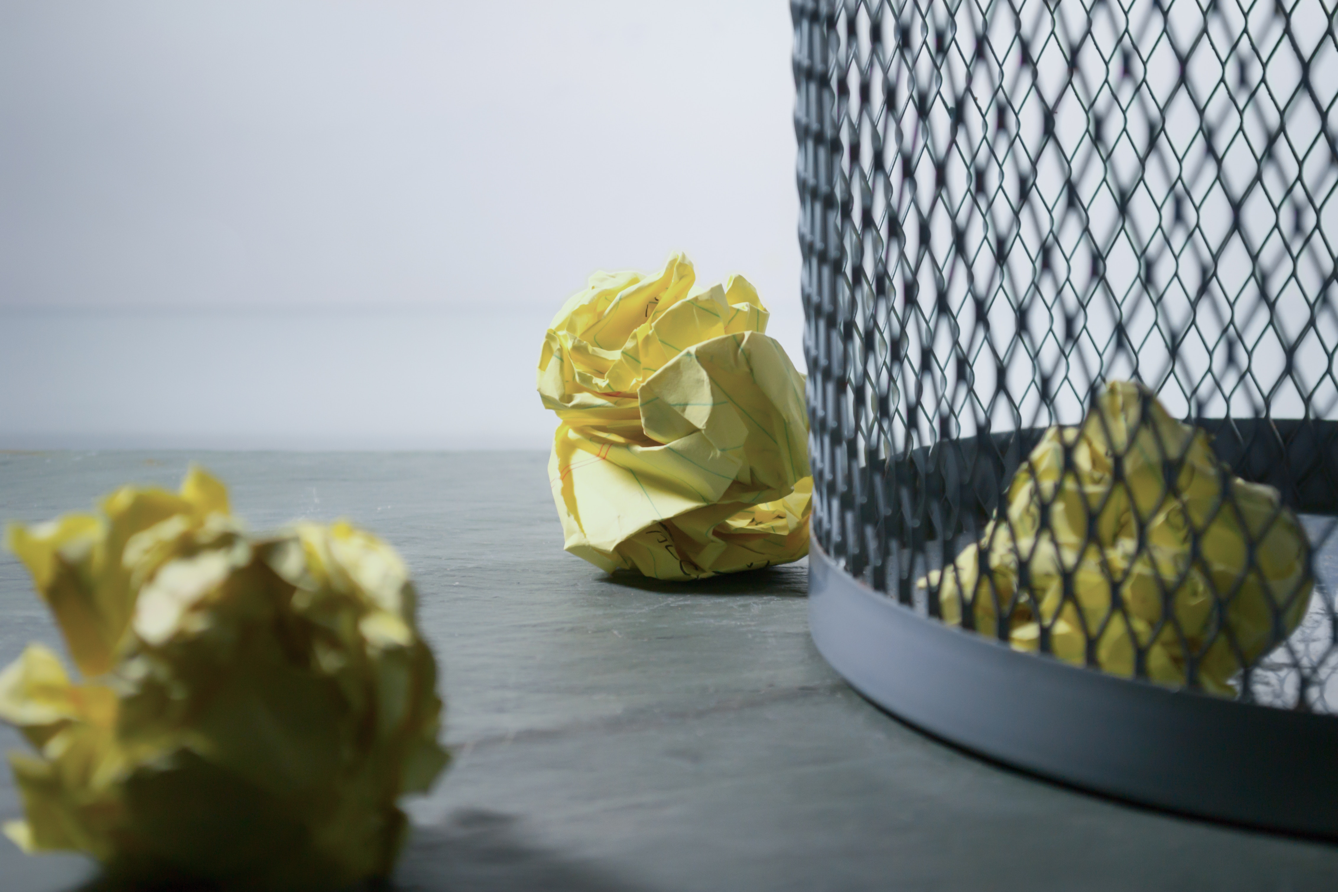 Image of a metal waste paper basket with crumpled papers both inside and outside.