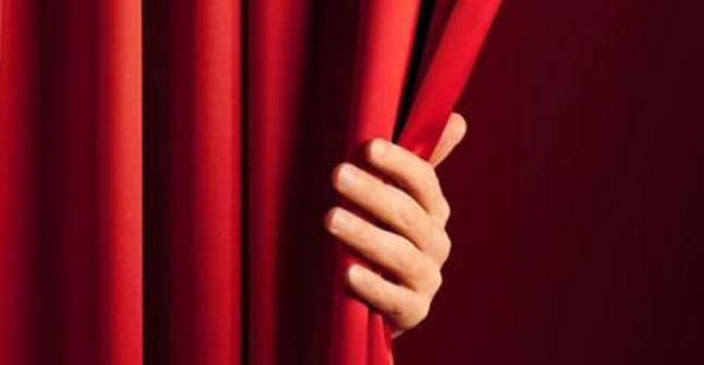 Image of a hand beginning to pull back a large red curtain.