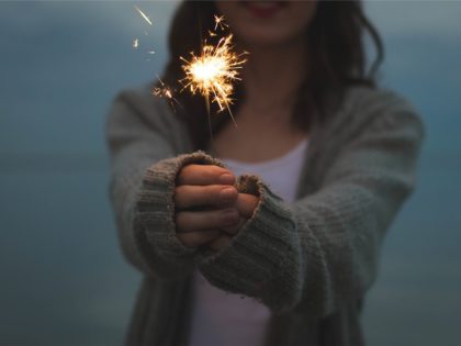Image of a younger woman holding a lit sparkler out in front of her.