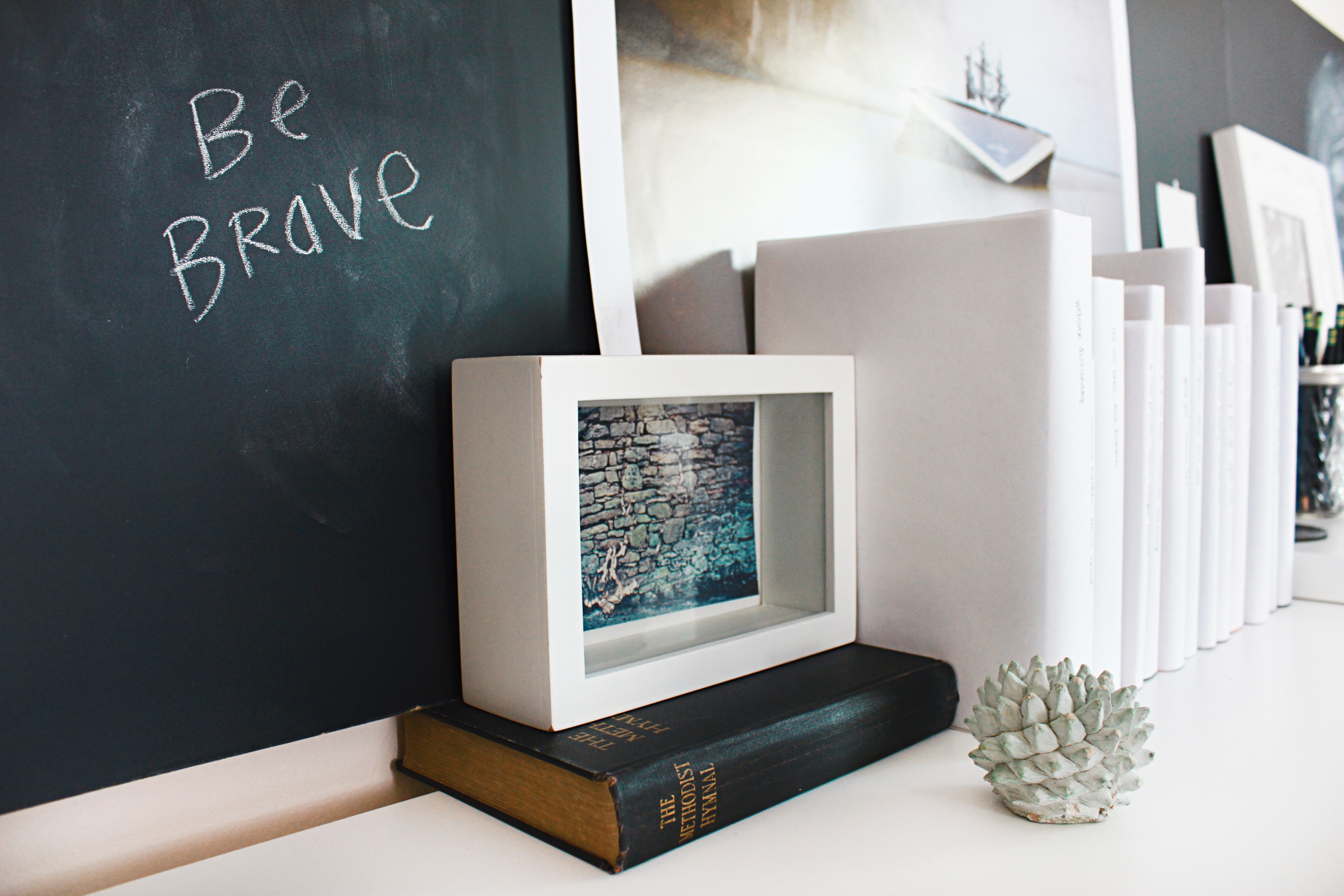 Image of a white bookshelf with numerous books and a small chalkboard with the words, "Be Brave" written in white chalk.