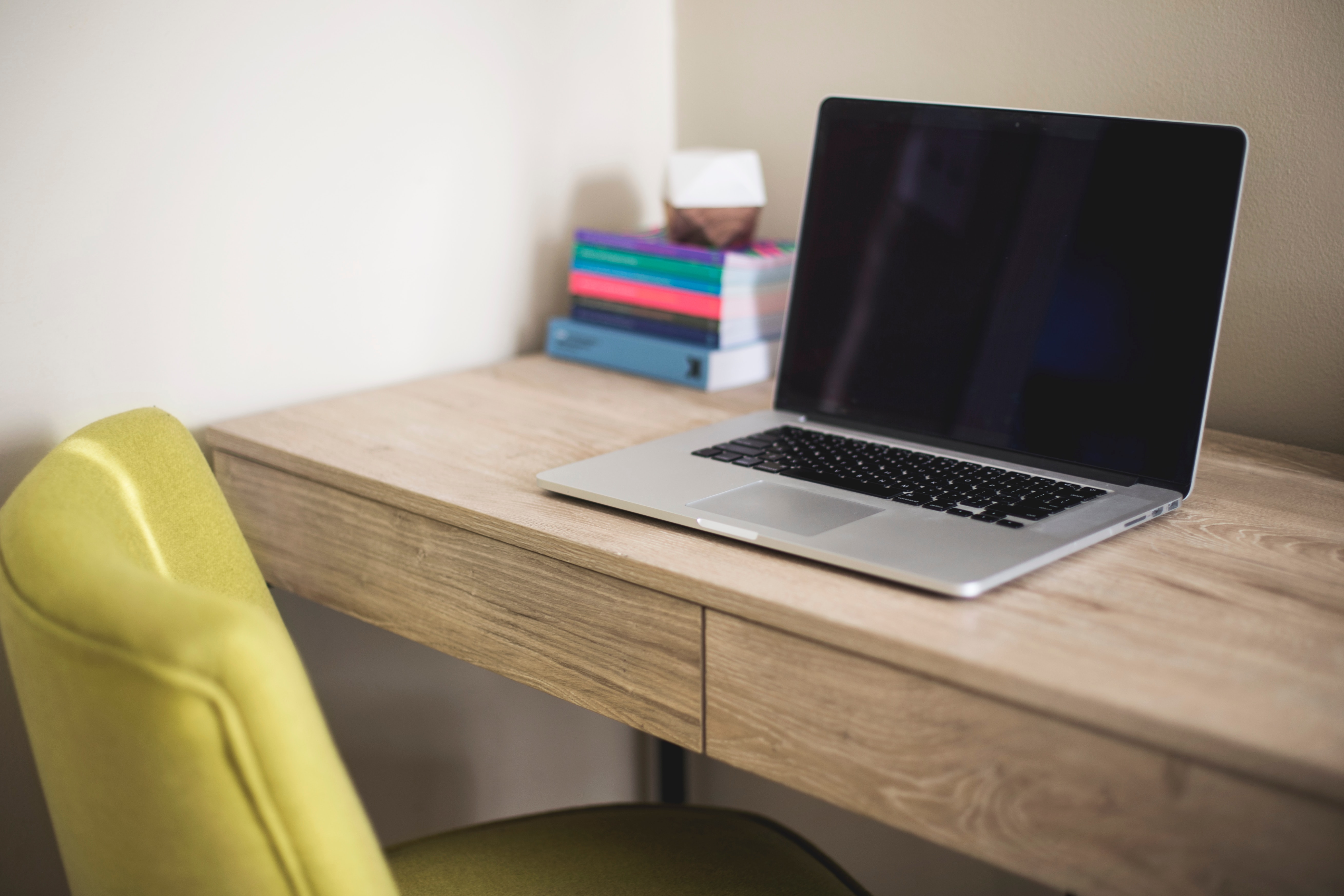 Image of a small room with a chair and desk, with an open laptop and books on it.