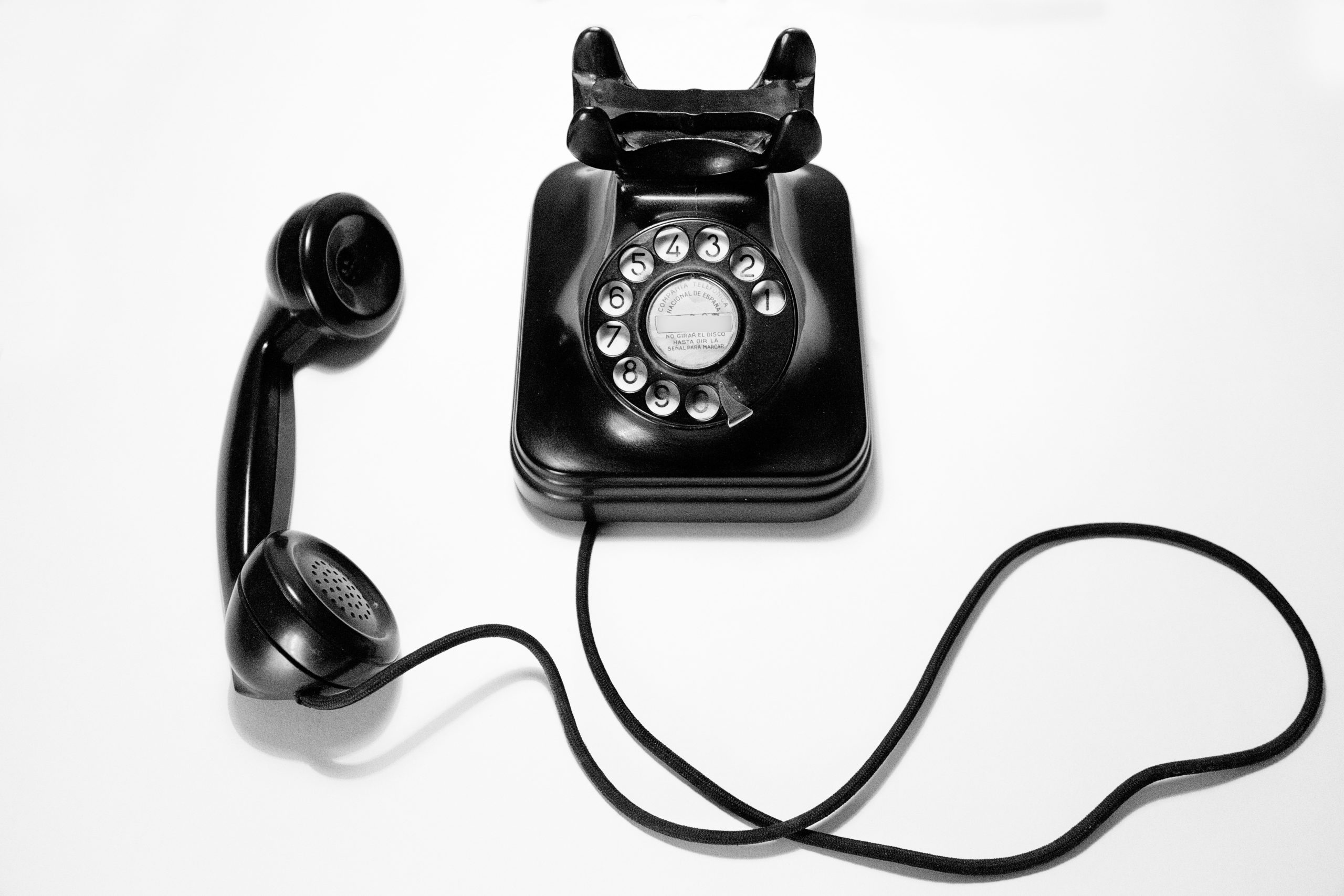 Image of a black rotary phone with the receiver off on a white background.