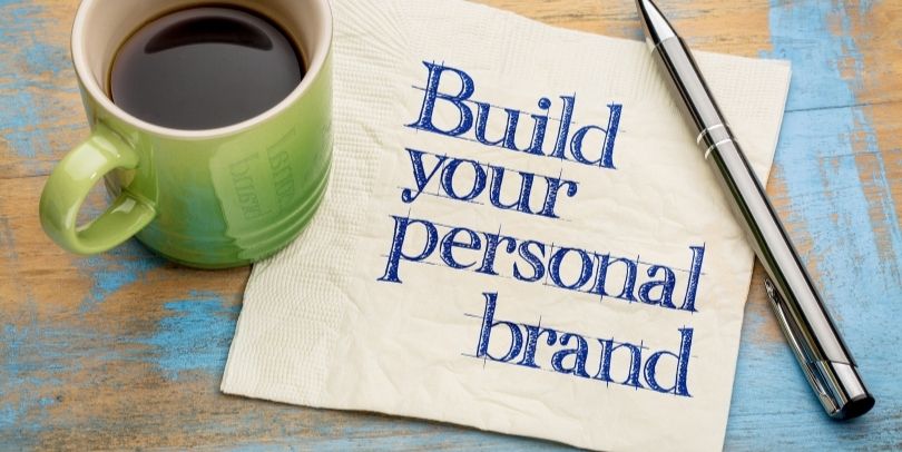 "Build your personal brand" advice handwritten on a napkin with a cup of espresso coffee and a silver pen.