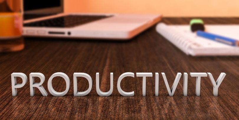 The word "PRODUCTIVITY" in letters on a wooden desk with laptop computer and a notebook.