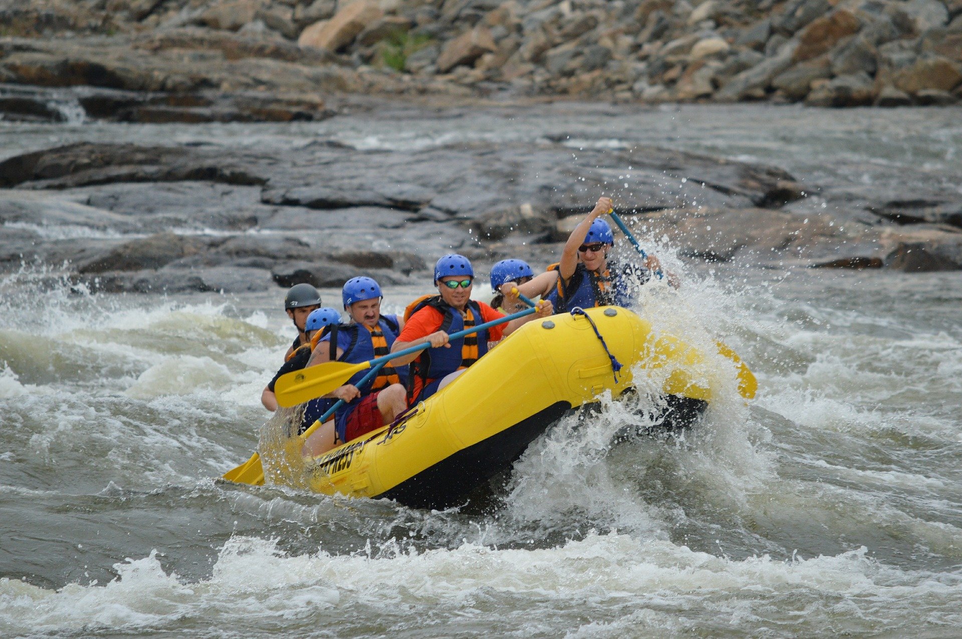 A group of people whitewater rafting on a river going up against waves of water.